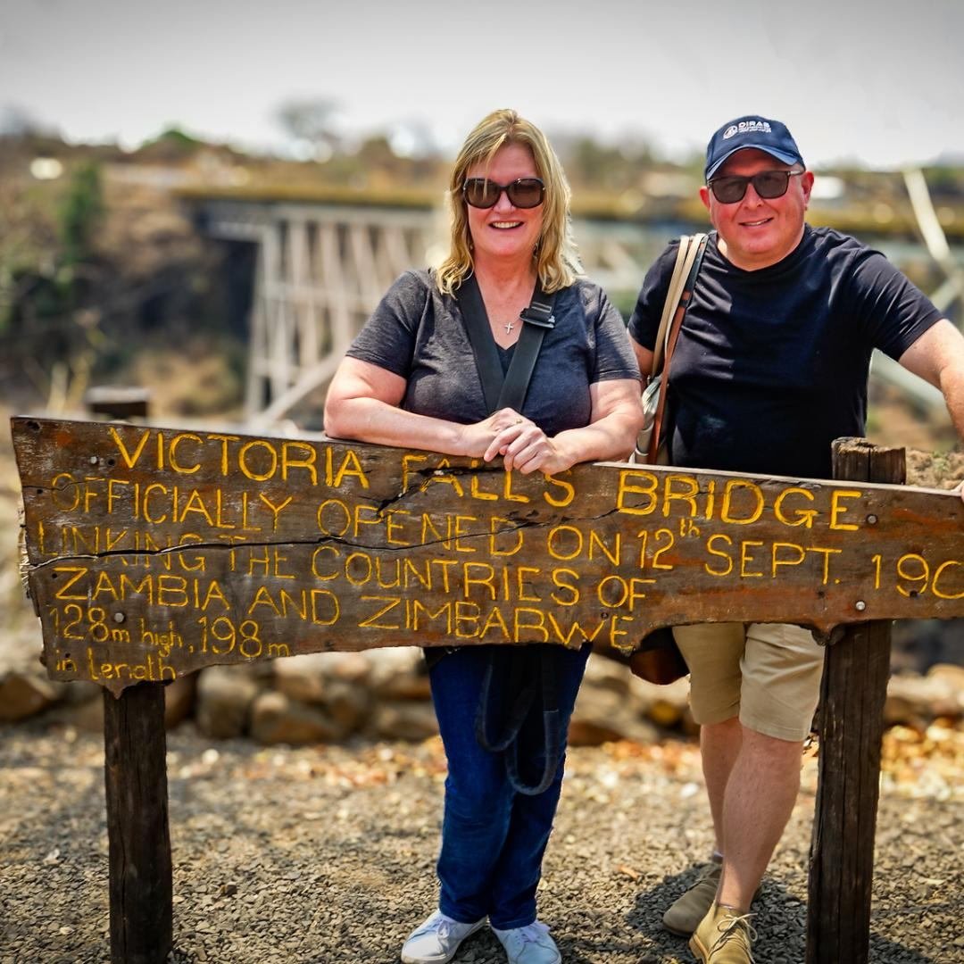 Travellers at the Victoria Falls Bridge border sign between Zimbabwe and Zambia