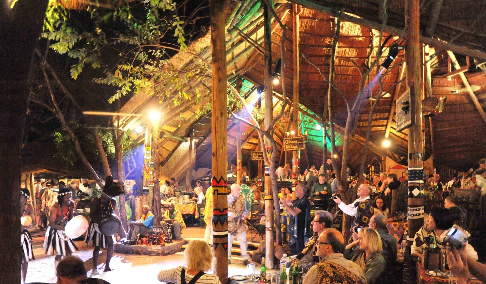 The Boma restaurant under thatch, lit up with guests dining in Victoria Falls