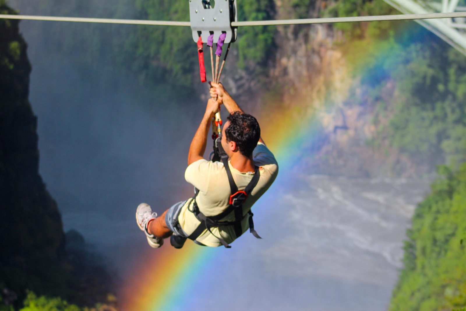 A rider on the Victoria Falls bridge slide with a rainbow in the gorge spray