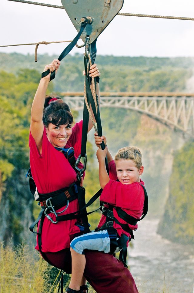An adult and child harnessed for the zipline with the bridge behind