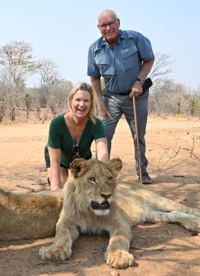 Visitors kneeling beside a young lion with a handler on the lion walk