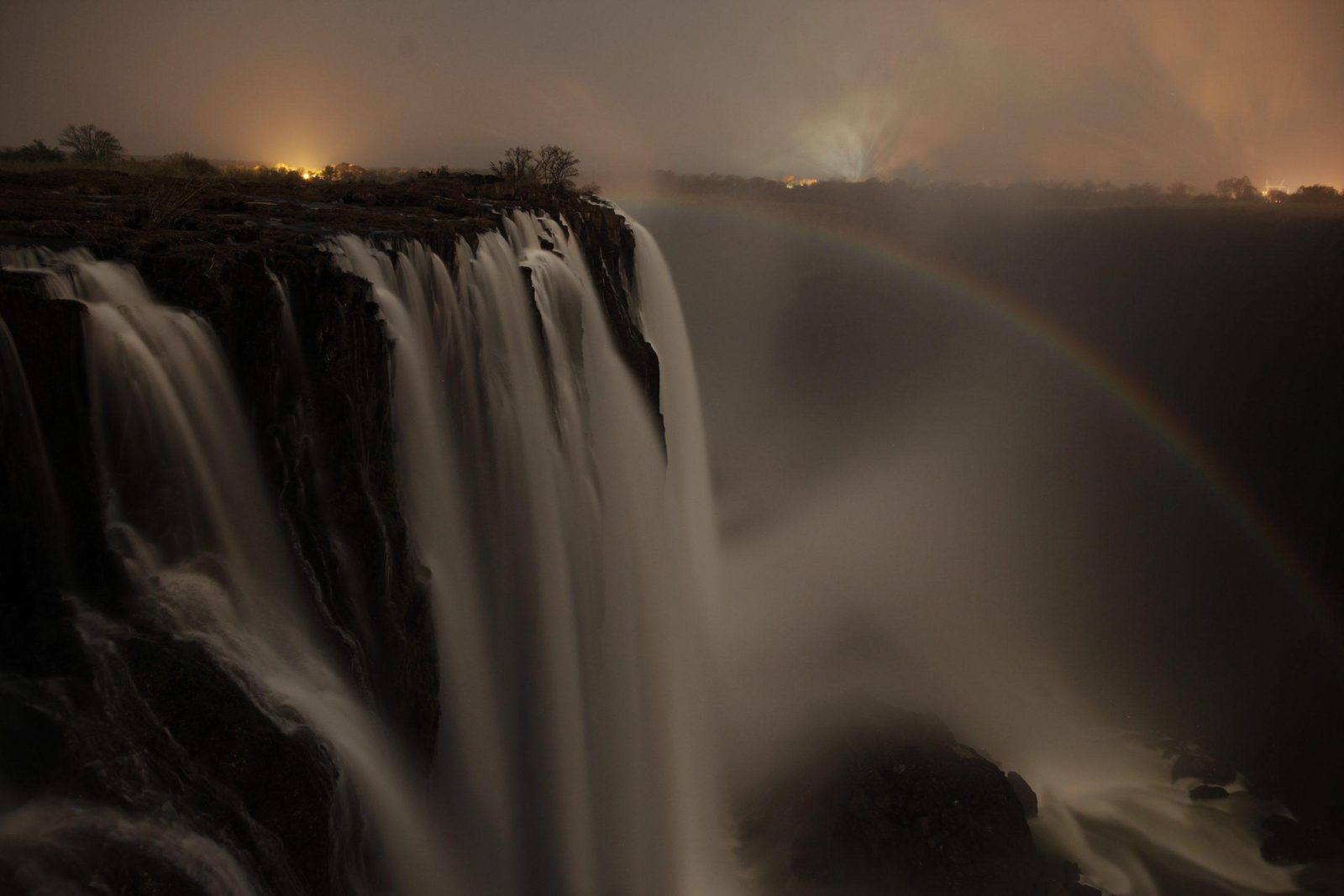 Victoria Falls lit by moonlight with spray rising from the gorge